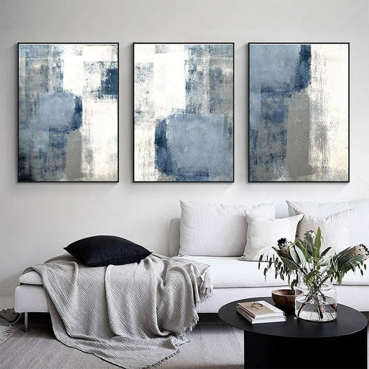 Three abstract art pieces on a wall above a white sofa with decorative pillows and a plant.