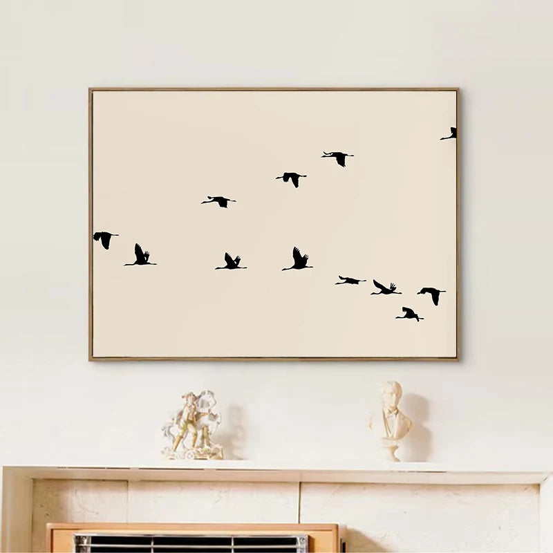Framed artwork with black bird silhouettes on a beige background, displayed on a wall above a wooden shelf.
