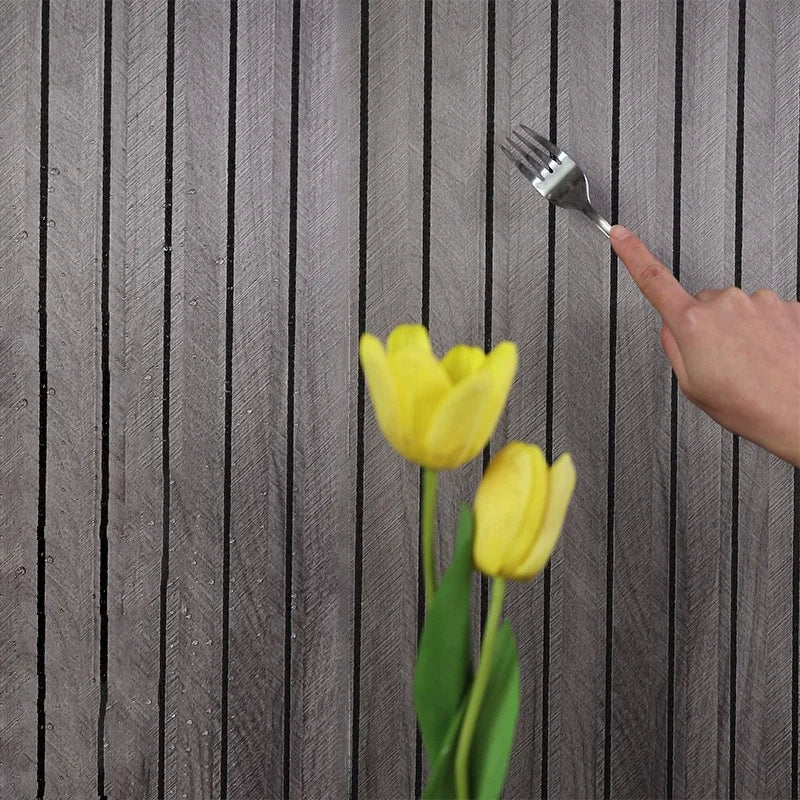 Person using a fork to scratch a gray wall with two yellow tulips in the foreground.