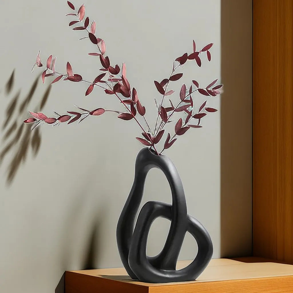 Black abstract vase with branches on a wooden surface against a neutral wall