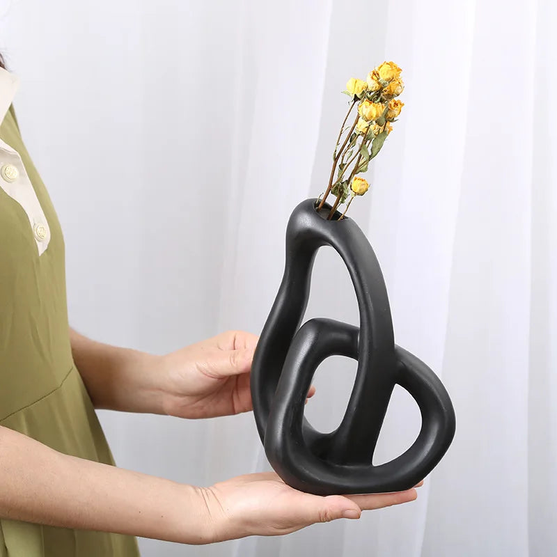 Person holding a modern black vase with yellow flowers against a white background