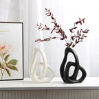 Two decorative vases, one white and one black, on a surface with a framed picture in the background.