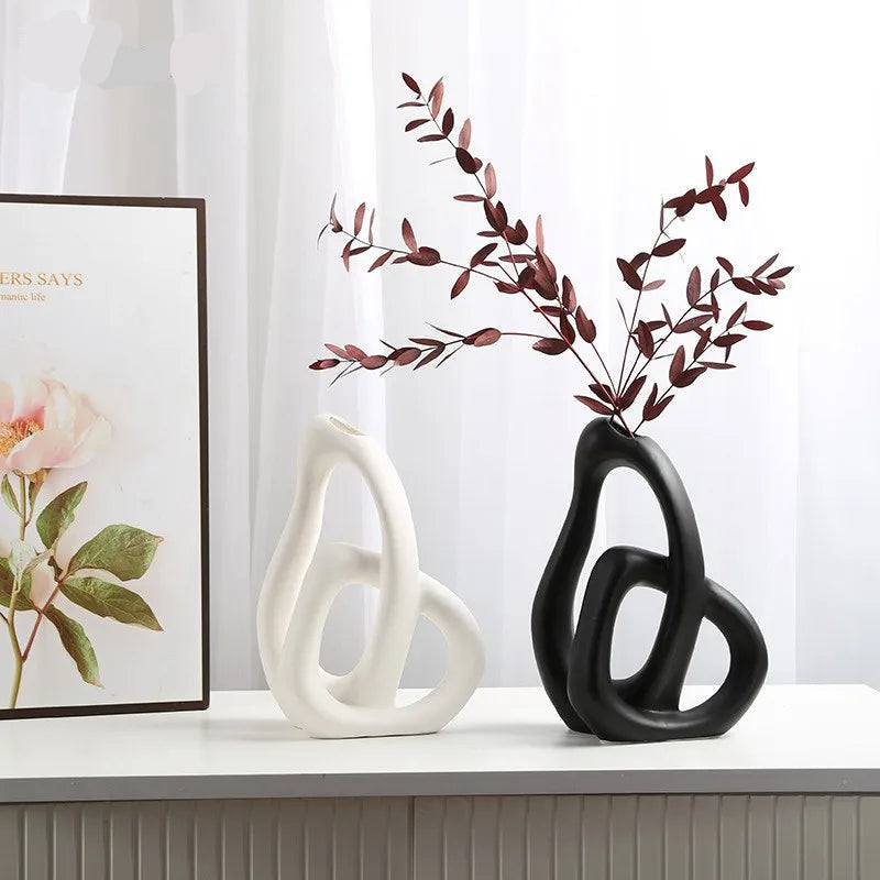 Two decorative vases, one white and one black, on a surface with a framed picture in the background.
