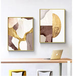 Two abstract art pieces with gold accents on a wall above a desk with a laptop.