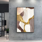 Abstract art piece with gold and brown elements on a gray wall.