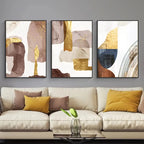 Three abstract art pieces on a wall above a beige sofa with colorful cushions.