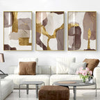 Three abstract art pieces in gold and brown frames on a wall above a white sofa.