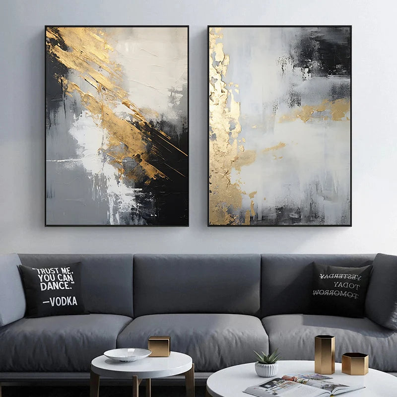 Two abstract art pieces in black, gold, and white above a gray sofa with decorative pillows.