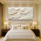 Neatly made bed with decorative pillows in a bedroom setting with wall art and lamps.