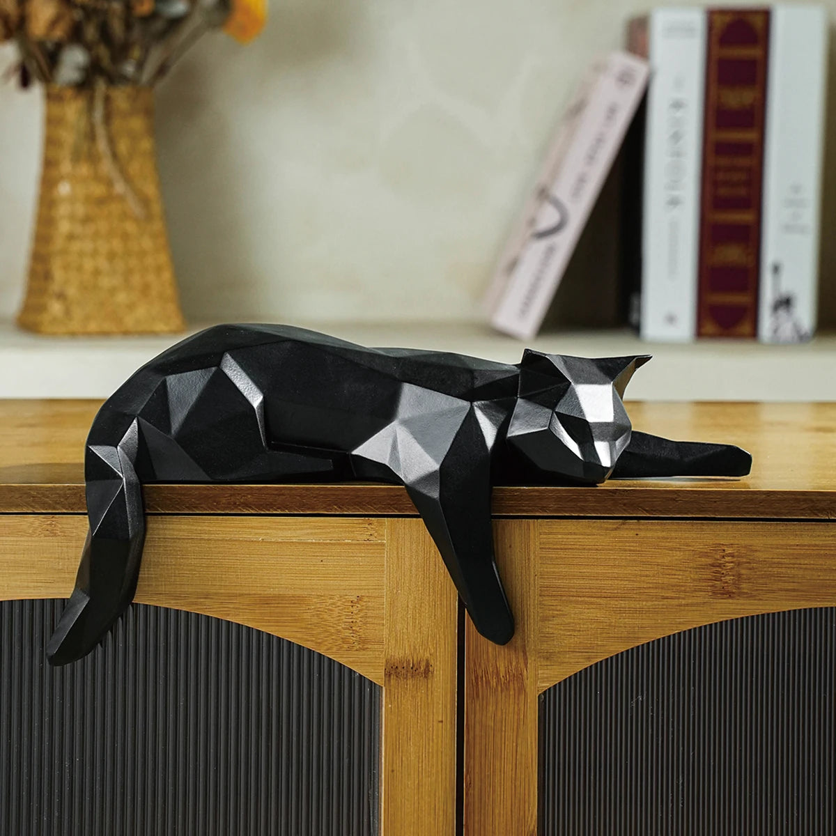 Black geometric cat sculpture on a wooden surface with books and a vase in the background