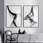 Two abstract black and white artworks on a wall with a chair and cabinet below.