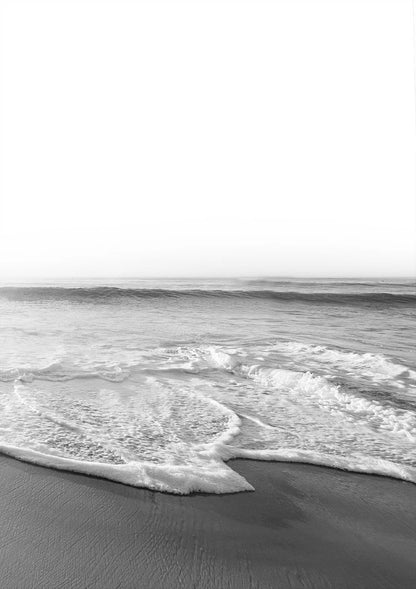 Black and white photo of a beach with waves crashing onto the shore.