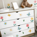 White dresser with floral and butterfly decals, teddy bear, and mirror on top.