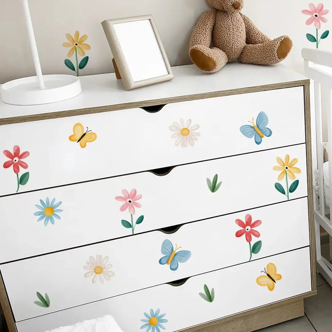 White dresser with floral and butterfly decals, teddy bear, and mirror on top.