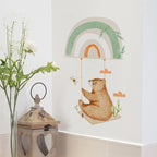 Children's wall decal of a bear and rainbow with a lantern and flowers on a white wall.