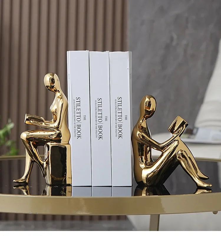 Gold abstract sculptures on a table with white books in the background