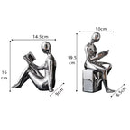 Two metallic sculptures of people sitting on boxes with dimensions indicated.