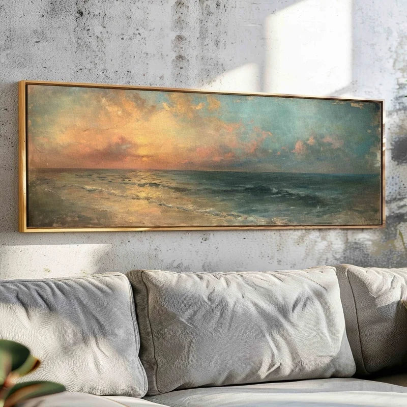 Framed painting of a sunset over water above a sofa with decorative pillows.