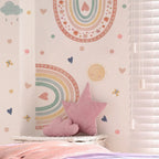 Children's room with pastel-colored wall design featuring rainbows, hearts, and stars, with a pink star-shaped pillow on a bed.