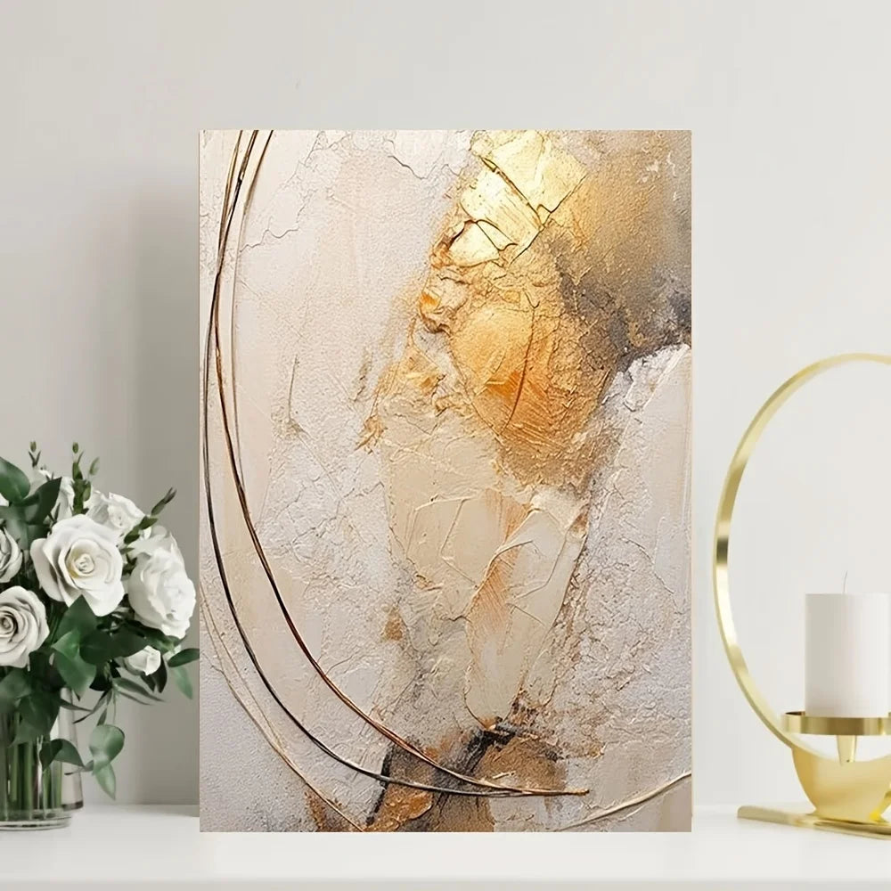 Abstract art piece with gold and beige tones on a white wall, accompanied by a vase of flowers and a gold lamp.