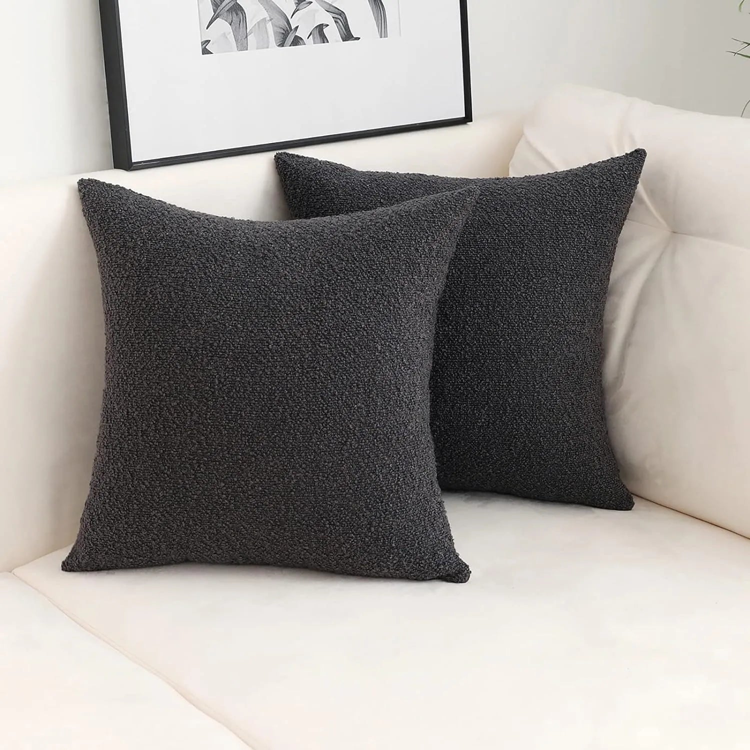 Two dark gray textured throw pillows on a white sofa with a framed picture in the background.