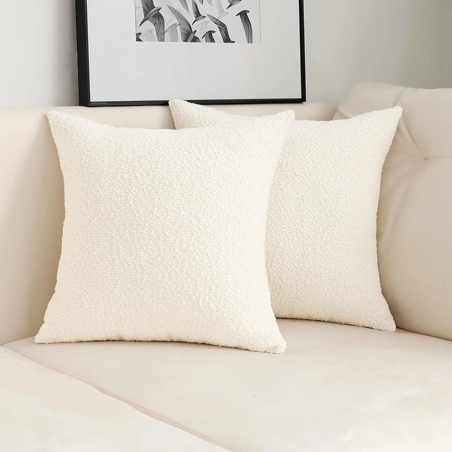 Two textured white pillows on a beige sofa with a framed black and white abstract art piece above.