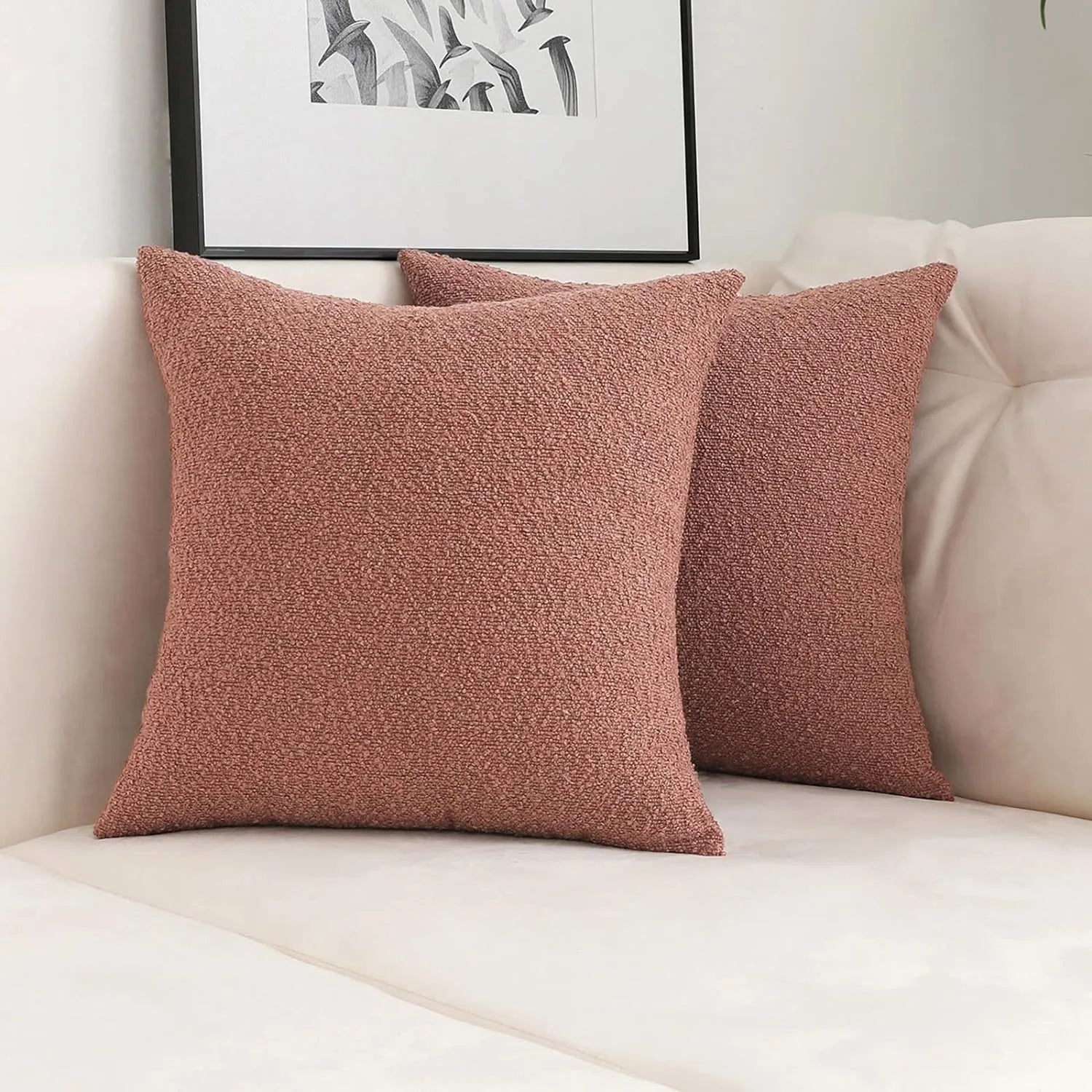 Two pink textured throw pillows on a beige sofa with a framed picture in the background.