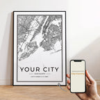 Framed city map poster on a wall with a hand holding a smartphone.