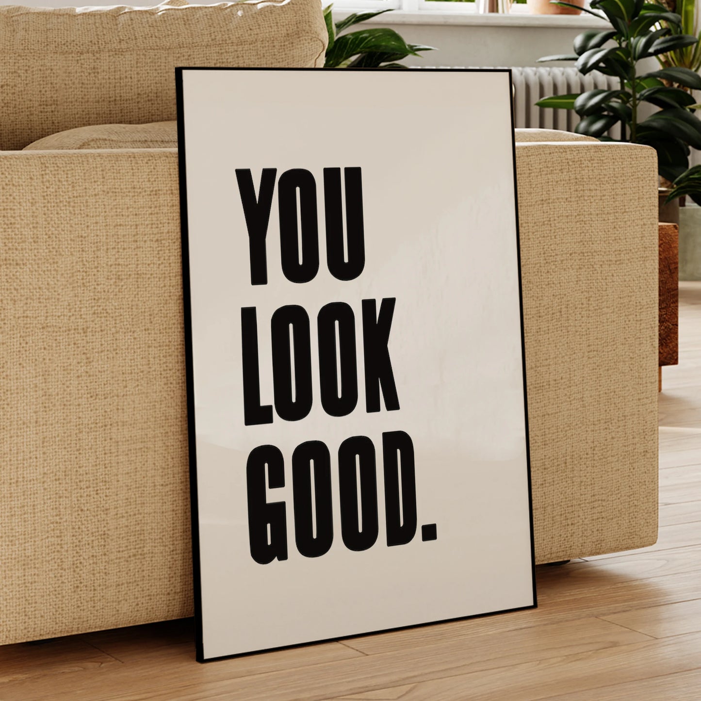 Poster with 'YOU LOOK GOOD.' text leaning against a beige sofa in a living room.