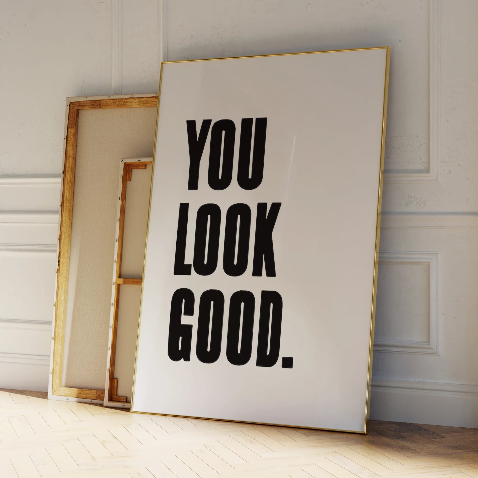 Framed poster with 'YOU LOOK GOOD.' text on a wooden floor.