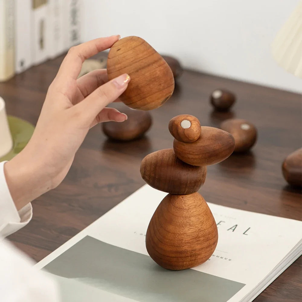 Wooden balance toy being held by a hand on a wooden surface with other toys in the background.