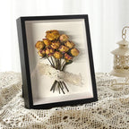 Dried yellow roses in a black frame on a lace surface with a white lantern in the background.