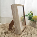 Wooden photo frame on a textured surface with a blurred background of flowers and curtains.