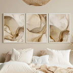 Three abstract wall art pieces in neutral tones above a bed with white bedding.