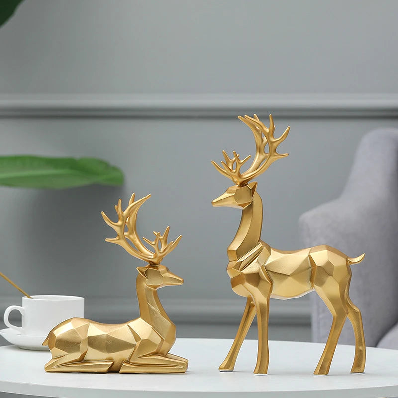 Two gold deer figurines on a white surface with a blurred background