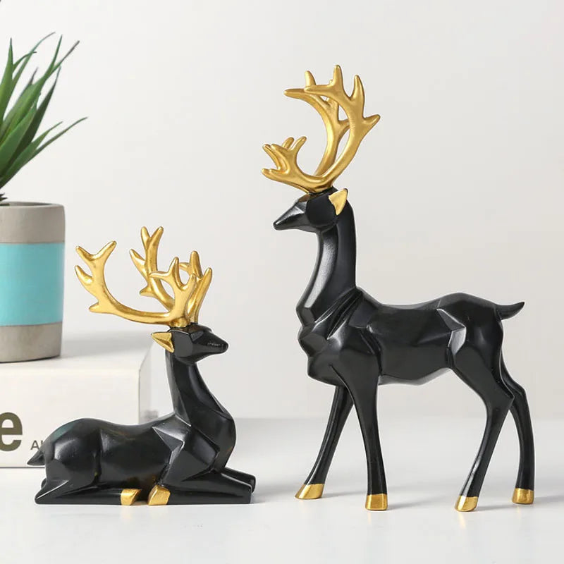 Two black deer figurines with gold antlers on a white surface.