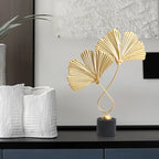 Gold leaf sculpture on a black base with white textured vases in the background