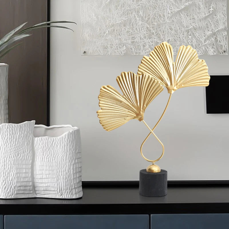 Gold leaf sculpture on a black base with white textured vases in the background