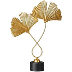 Decorative gold sculpture of two leaves on a black base against a white background