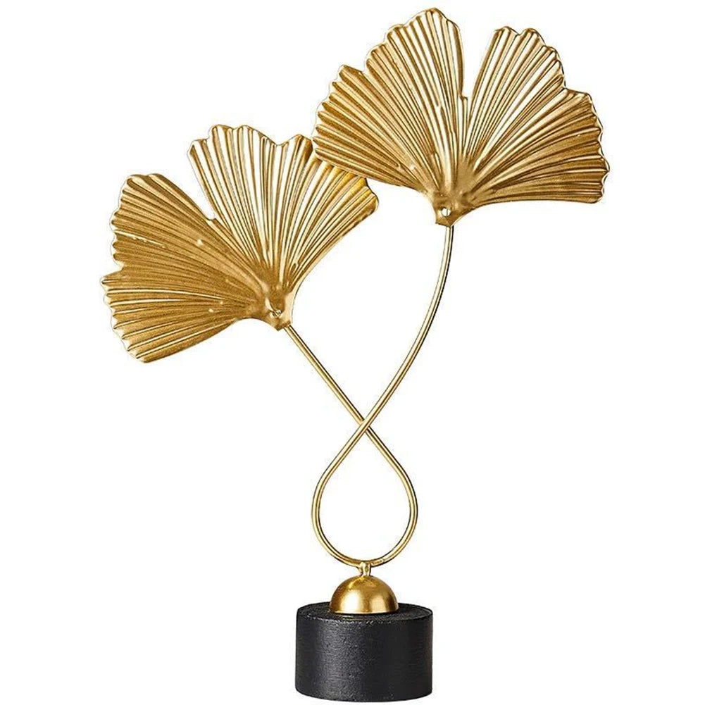 Decorative gold sculpture of two leaves on a black base against a white background