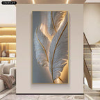 A vertical wall art piece featuring large white feathers with warm gold highlights, displayed in a modern interior hallway with a staircase and built-in shelving visible.