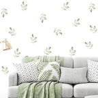 Gray sofa with decorative pillows and a green blanket, featuring leaf wall decals on a white background.