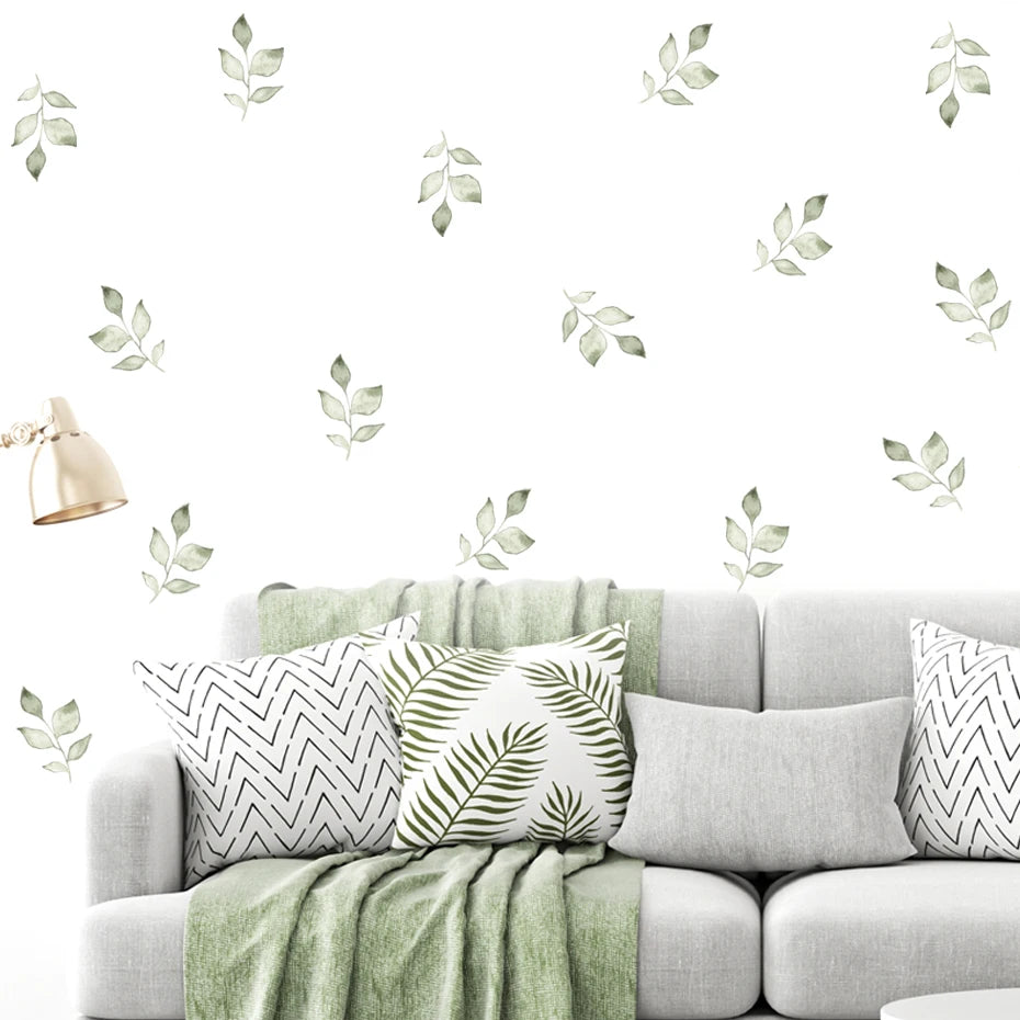Gray sofa with decorative pillows and a green blanket, featuring leaf wall decals on a white background.