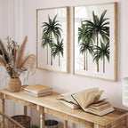 Two framed palm tree prints on a wall above a wooden console table with books and decor.