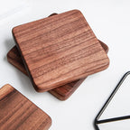 Three square wooden coasters with rounded corners, stacked and overlapping on a white surface. The coasters have a warm reddish-brown wood grain finish.