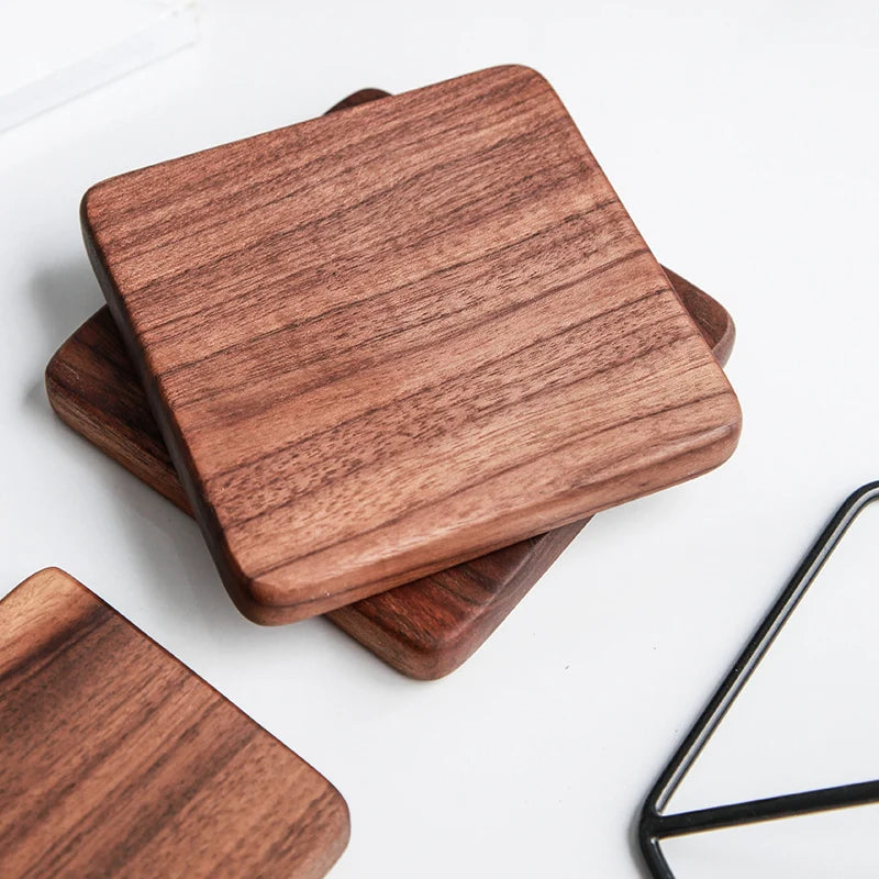 Three square wooden coasters with rounded corners, stacked and overlapping on a white surface. The coasters have a warm reddish-brown wood grain finish.