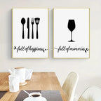 Two framed prints with kitchen utensils and wine glass silhouettes on a wall above a table.