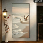Beach scene with two birds flying over sand and water, framed on a wall.