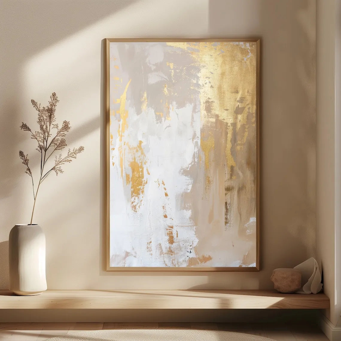 Abstract art piece in a gold frame on a wall with a vase and decorative object below.