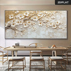 Large rectangular wall art showing a 3D-effect white magnolia blossom branch with gold leaf texture, displayed above a dining table in a modern interior. A small '2D/FLAT' label appears in the top-right corner.